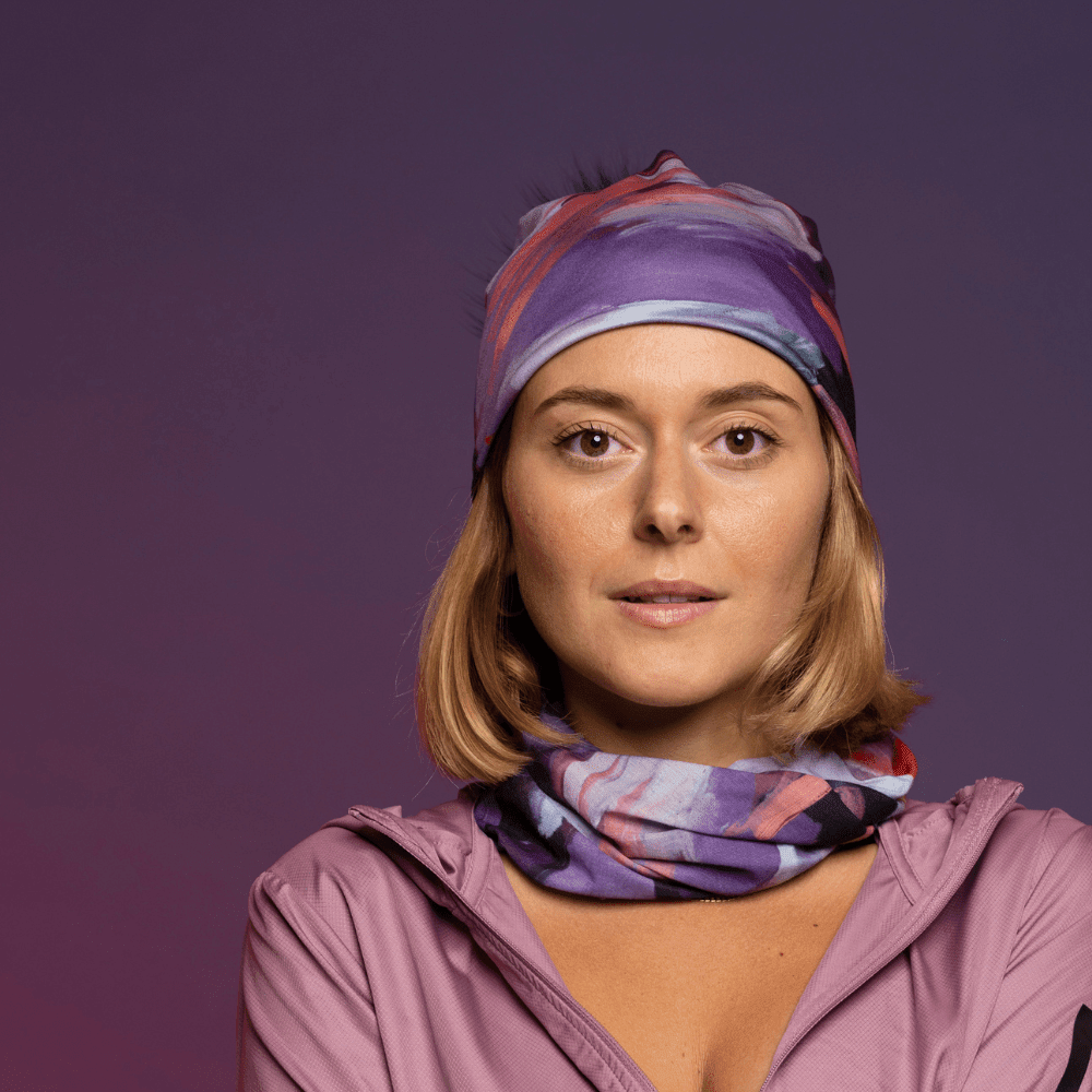 A woman wears a matching beanie and neck tube with a floral art print, posing against a purple background.