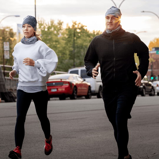 Un homme et une femme courant dehors au coucher du soleil, portant tous deux des tuques et cache-cous assortis à rayures abstraites.