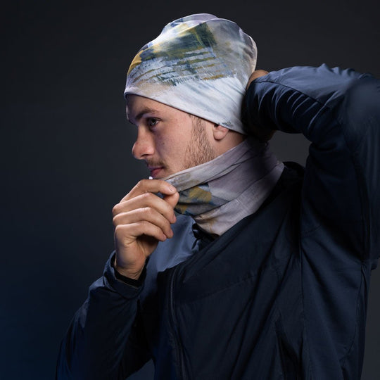 Un homme enfilant la Tuque Unisexe Sable tout en portant un cache-cou multifonctionnel assorti.