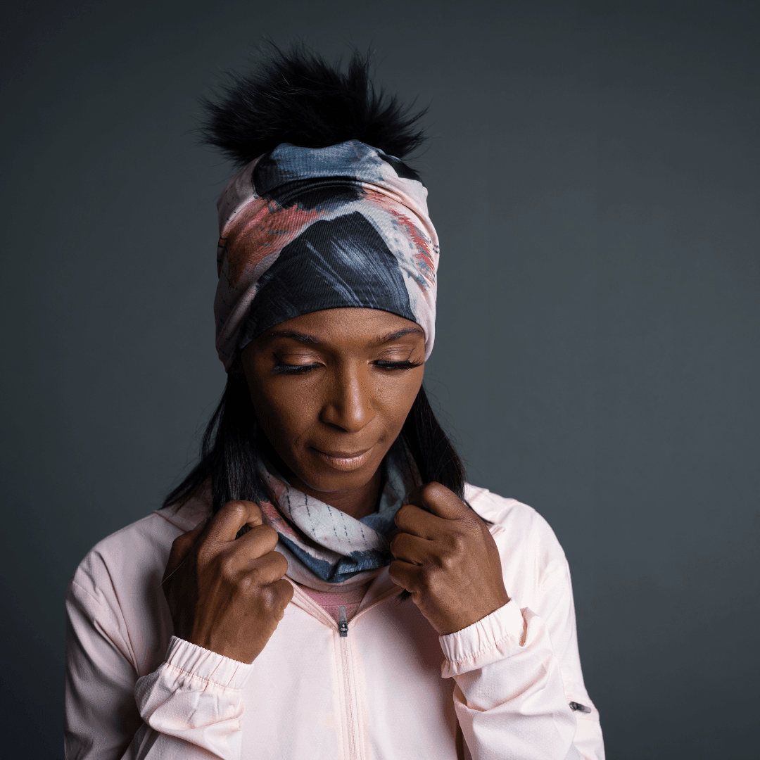 Femme portant la tuque Vie en Rose comme bandeau, avec le pompon noir visible, et ajustant un cache-cou assorti.