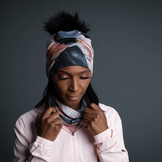 Femme portant la tuque Vie en Rose comme bandeau, avec le pompon noir visible, et ajustant un cache-cou assorti.