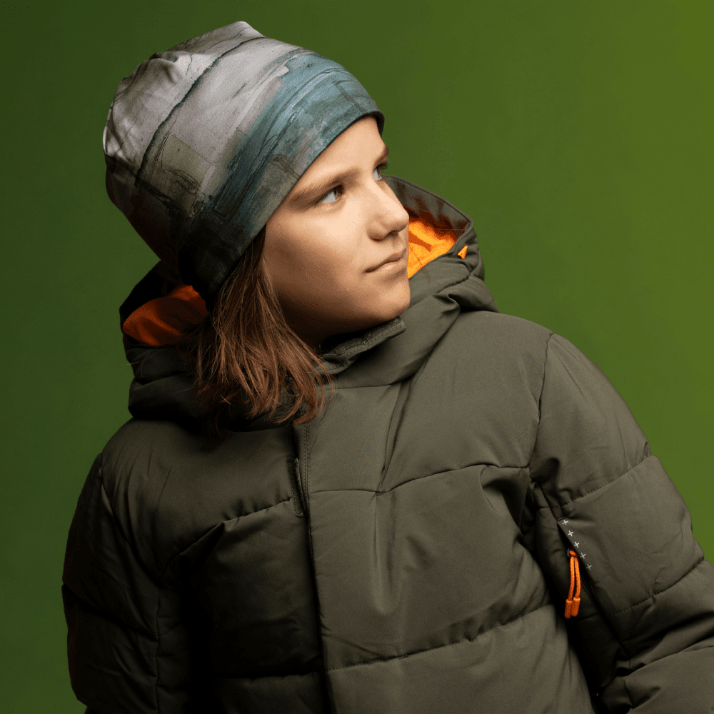 Enfant portant la Tuque Murale et une veste d'hiver verte, regardant de côté.