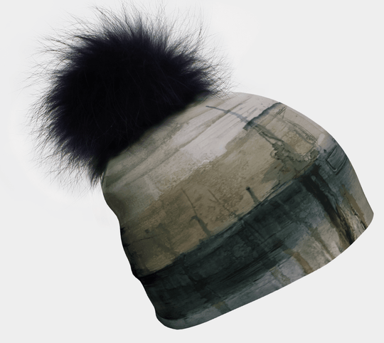 Une tuque abstraite verte et grise avec un grand pompon noir en fourrure est présentée sur fond blanc.
