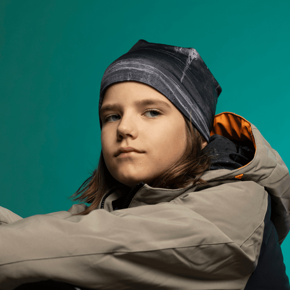 Enfant portant la tuque Wall Black avec un manteau gris et orange, profil rapproché sur fond studio sarcelle