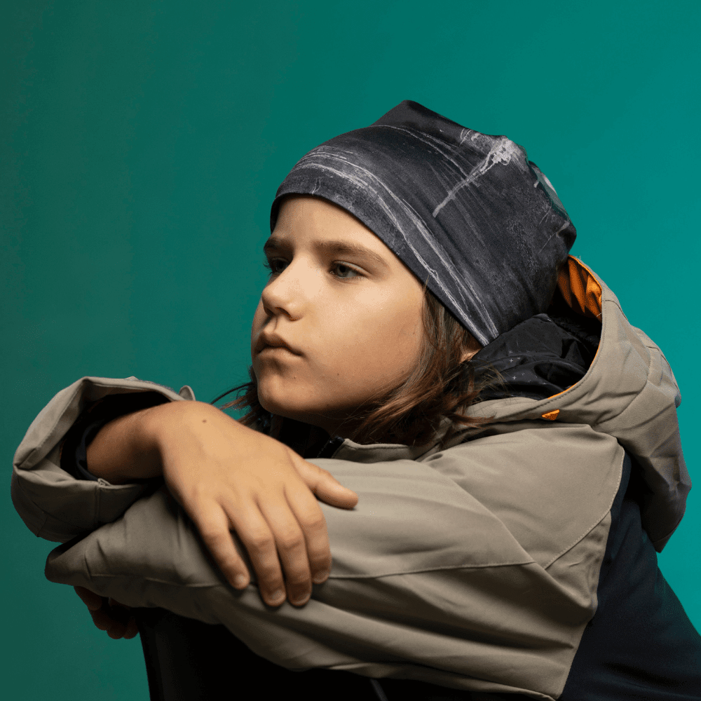 Enfant en tuque Wall Black de profil, regard au loin — silhouette complète sur fond sarcelle