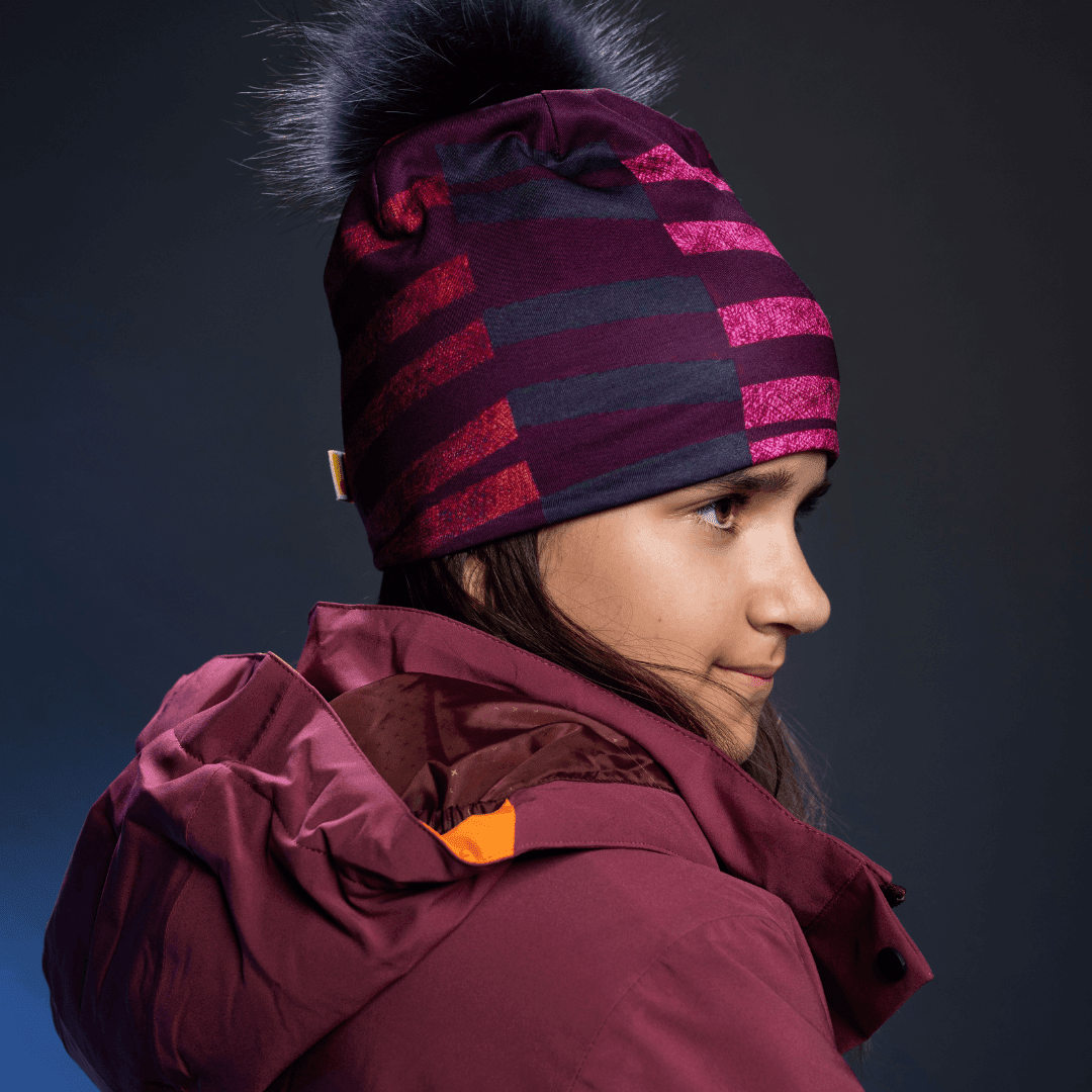 Jeune femme portant une tuque rayée violette et rose avec un pompon noir, regardant sur le côté.