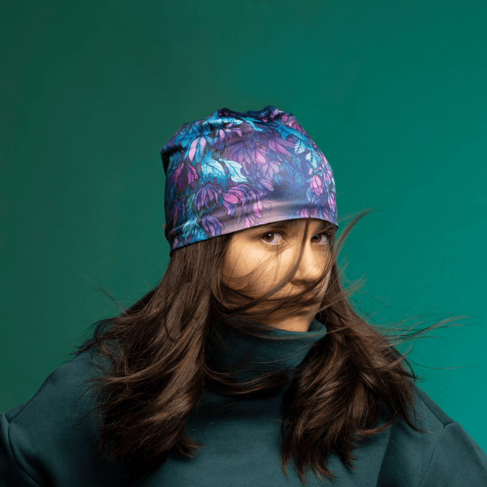Une jeune femme aux longs cheveux foncés portant la tuque Wisteria et un col roulé bleu sarcelle foncé, ses cheveux volant autour de son visage.