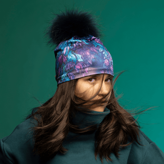 Jeune femme portant la tuque à pompon Wisteria, ses cheveux au vent sur fond turquoise.
