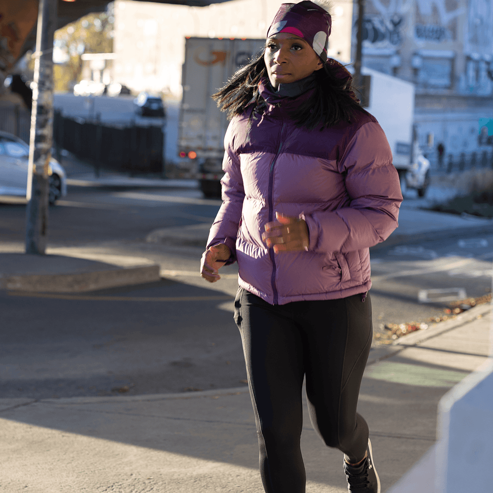 Femme courant dehors portant une veste d'hiver violette et une tuque magenta avec un pompon gris.