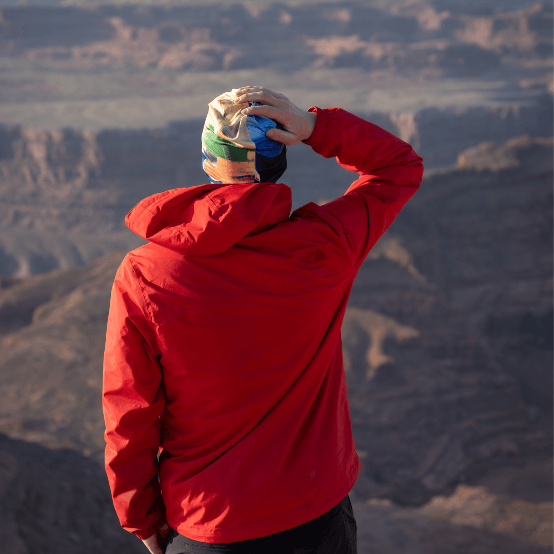 Homme en veste rouge portant la tuque à art abstrait, contemplant un paysage montagneux.