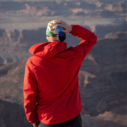 Homme en veste rouge portant la tuque à art abstrait, contemplant un paysage montagneux.