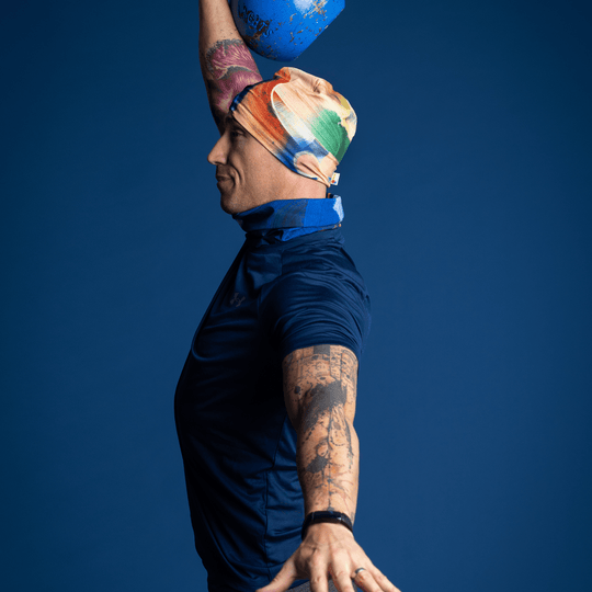 Homme portant la tuque à art abstrait jaune et bleu et le cache-cou assorti, effectuant un épaulé-jeté avec kettlebell.