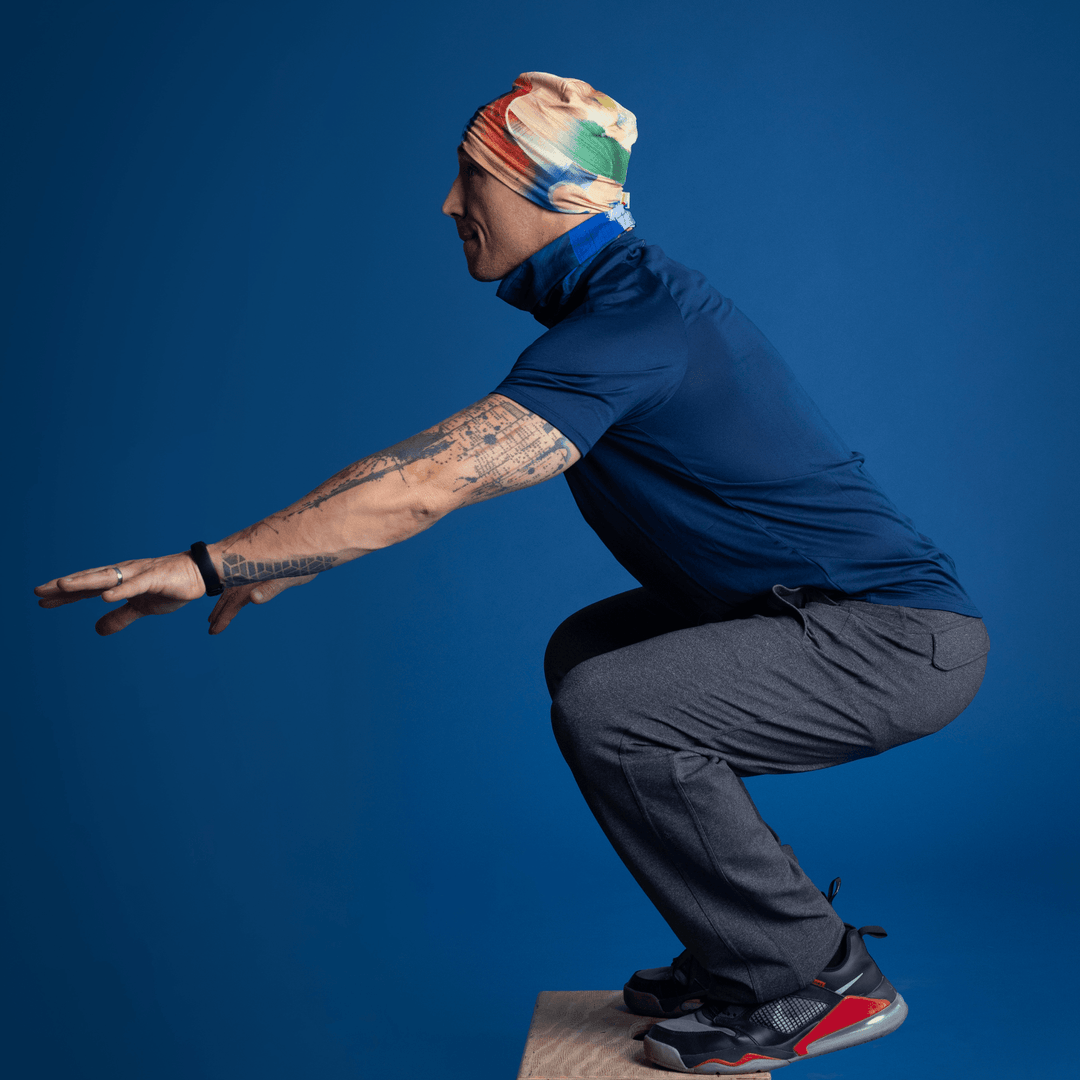 Homme portant la tuque et le cache-cou à art abstrait, effectuant un exercice de squat.