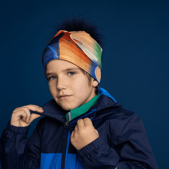 Jeune garçon portant la tuque jaune et bleue avec pompon en fausse fourrure marine amovible, stylisée avec une veste.