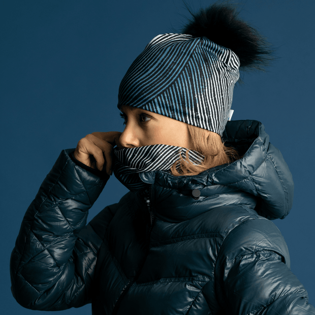 Big Fur Removable black pom beanie for women, side view of a woman putting her her abstract multifonctional tube to cover her face. 