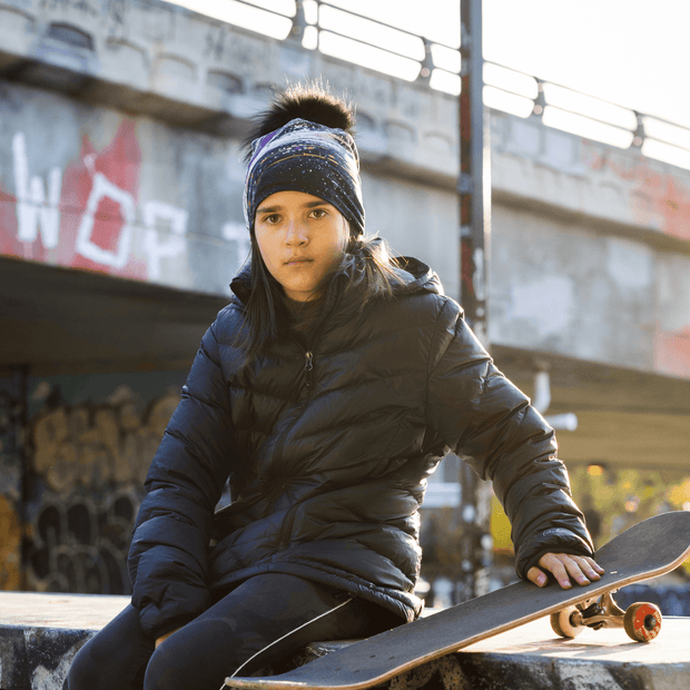 Girls in street with a skateboard. She wears the Lalita's Art Shop Abracadabra beanie model, with an abstract pattern on bamboo fabrics and a detachable black pompom