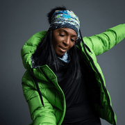 Beautiful black woman dancing. She wears a green coat, and the jellyfish hat illustrated by the young artist Mégane Fortin. The hat is made of bamboo, black with abstract patterns and a black pompom.