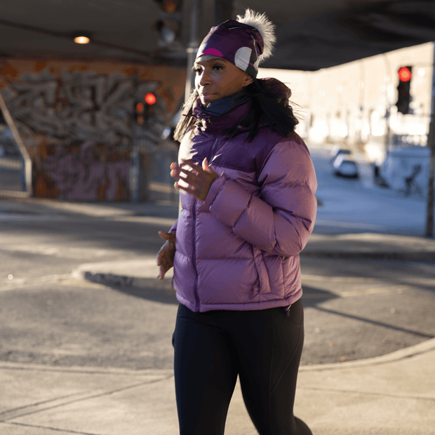 Young sporty woman running in the street. She is wearing the four seasons Umbrella Magenta beanie with removable grey pom-pom illustrated by Valéry Goulet. Lalita's Art shop hats are illustrated by Quebec artists and are designed for all outdoor and sports activities.